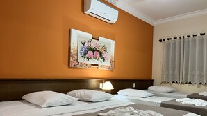 Une chambre d’hôtel avec deux lits, une tête de lit, un climatiseur fixé au mur et un tableau représentant des fleurs.