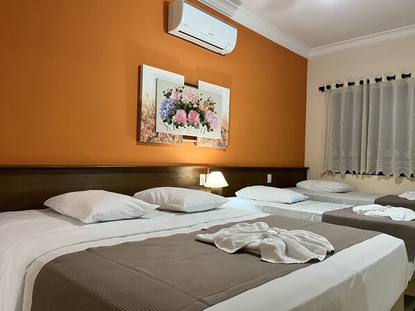 Habitación de hotel con dos camas, cabecera, aire acondicionado de pared y un cuadro de flores.