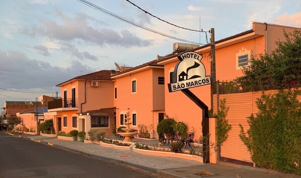 A hotel named "Hotel São Marcos" with a signboard, a fountain, and a well-maintained garden.