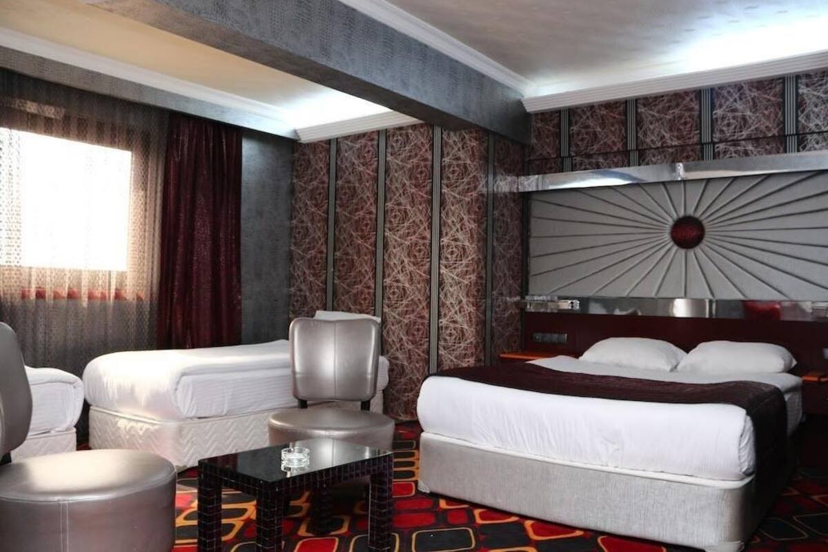 A hotel room with two beds, a seating area with a table, and a large wall-mounted headboard.