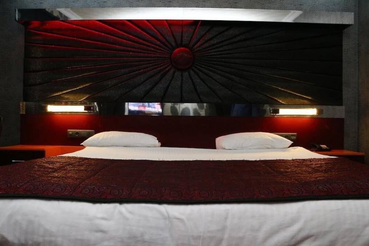 A bed with a red headboard, white bedding, and two bedside tables with lamps.