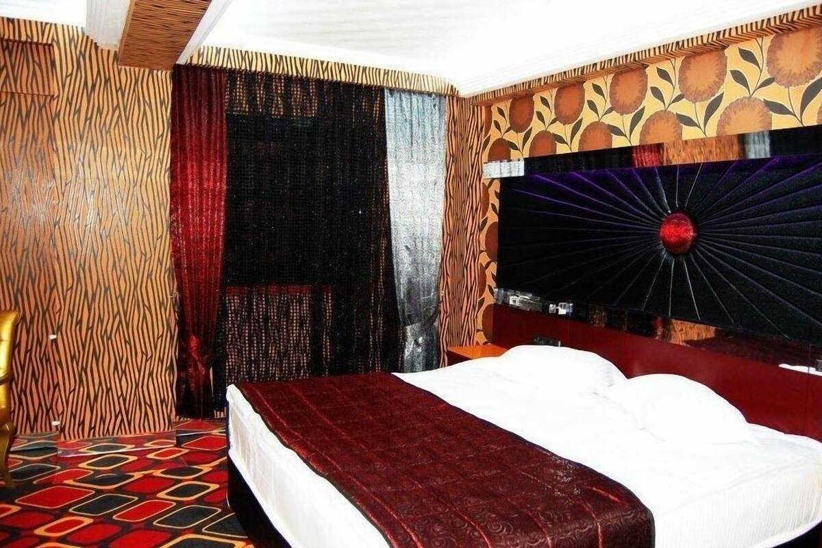 A hotel room with a patterned wall, a large bed with a red bedspread, and a decorative headboard.