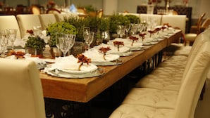 A long dining table set with white plates, glasses, and decorative flowers. - Lider Hotel Ituiutaba (Ituiutaba)