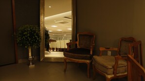 A hallway with a large mirror reflecting a well-lit room, two wooden chairs, and a potted plant. - Lider Hotel Ituiutaba (Ituiutaba)