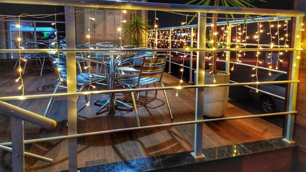 Un comedor con un separador de vidrio, sillas de metal y luces colgantes.