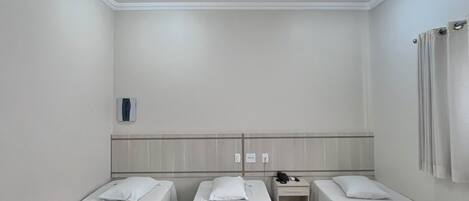 Habitación de hotel con tres camas individuales, ventilador de techo, unidad de aire acondicionado y mesita de noche con teléfono.