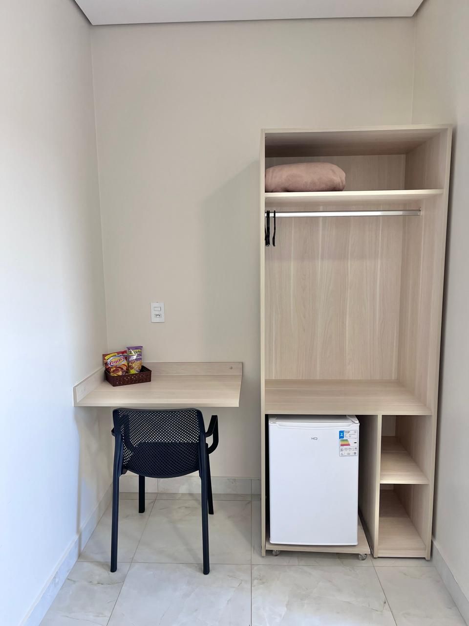 Une pièce de taille modeste, comprenant un petit bureau, une chaise et un mini-réfrigérateur blanc.