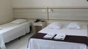 Habitación de hotel con dos camas individuales, una cama más grande, una mesita de noche con teléfono y un panel de control en la pared.