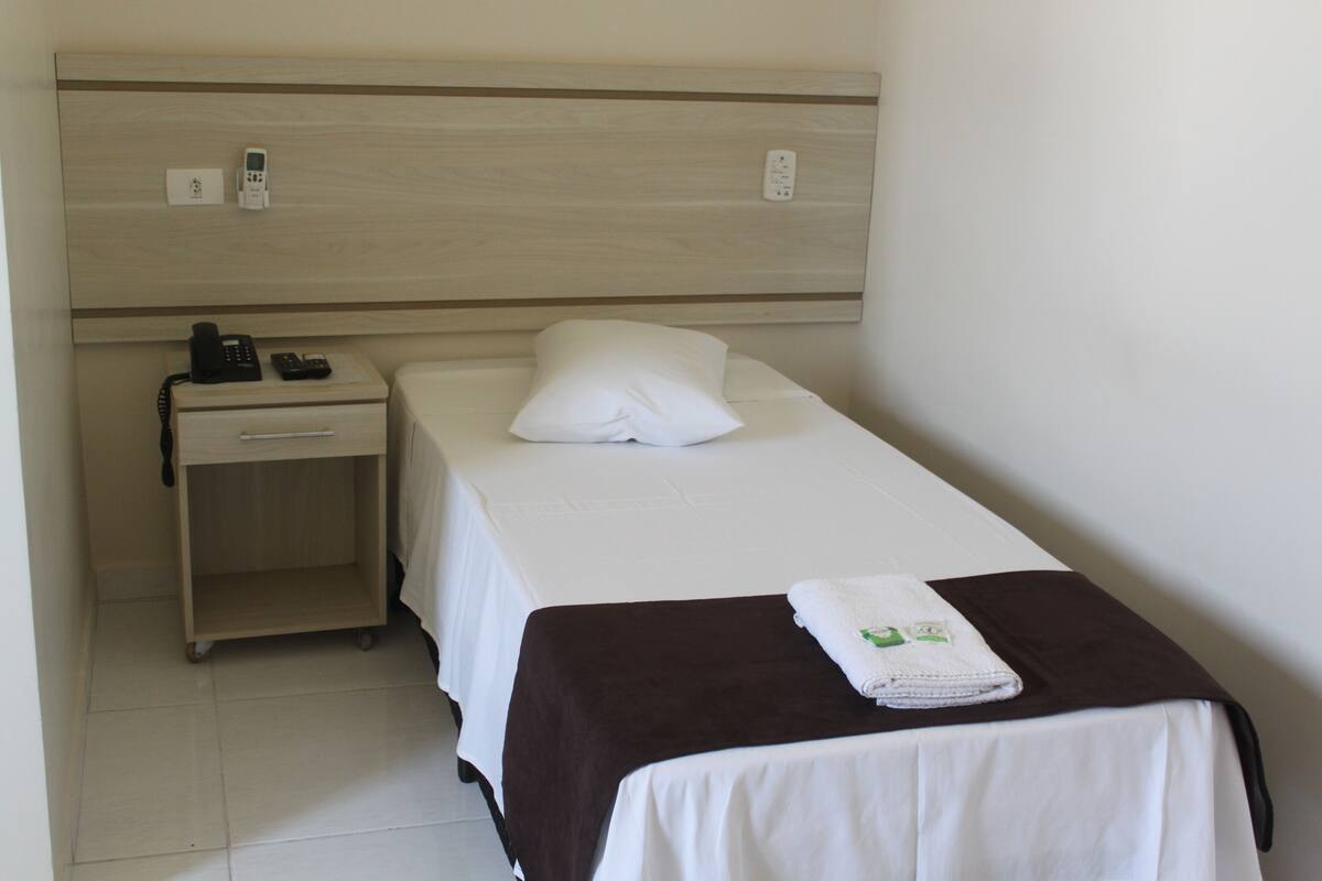 A hotel room with a single bed, a bedside table with a phone, and a small cabinet.