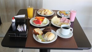 Una mesa de desayuno con platos de comida, un vaso de jugo, una taza de café y un holder para servilletas.