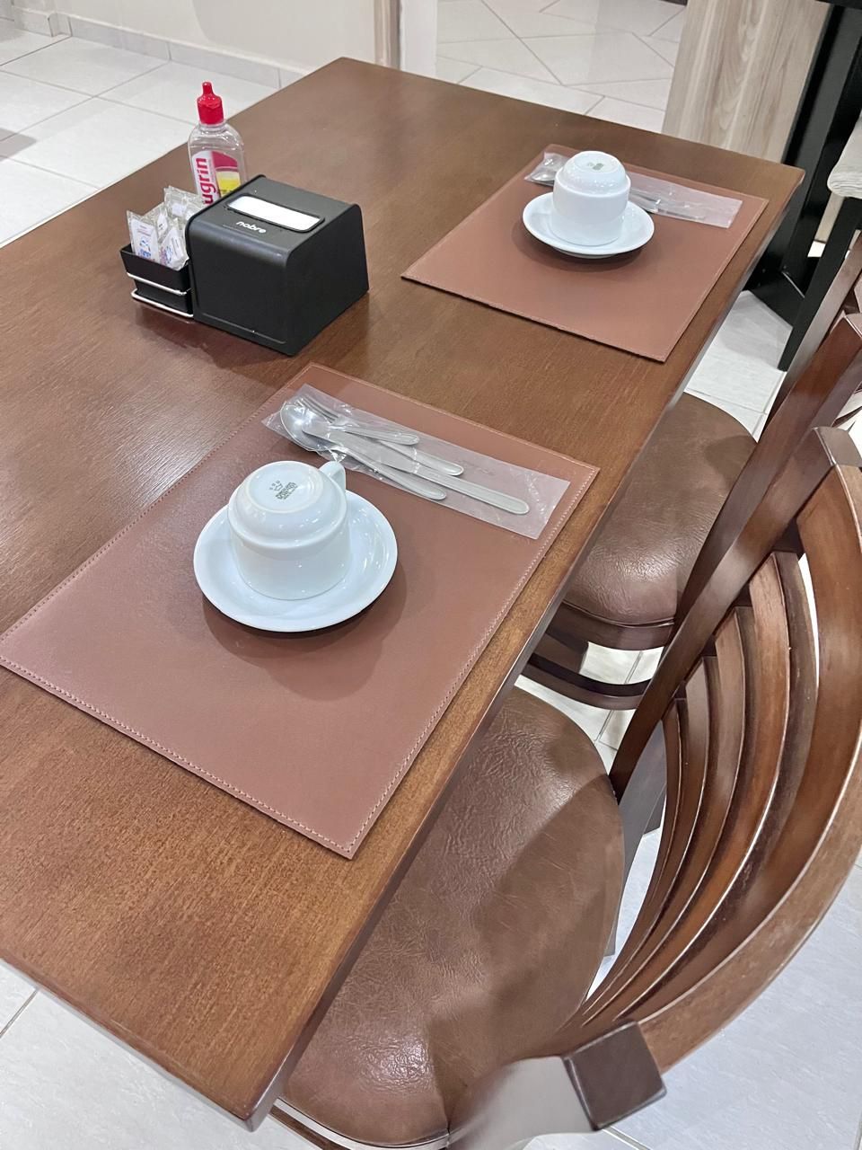 A dining table with placemats, a white teapot, and a bottle of hand sanitizer.