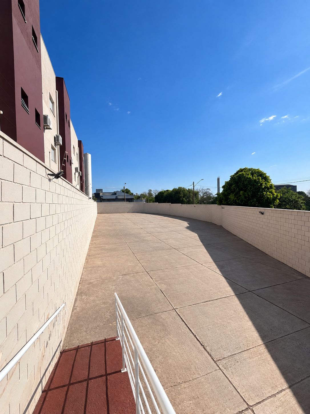 A paved walkway with a brick wall on one side and a clear blue sky above.