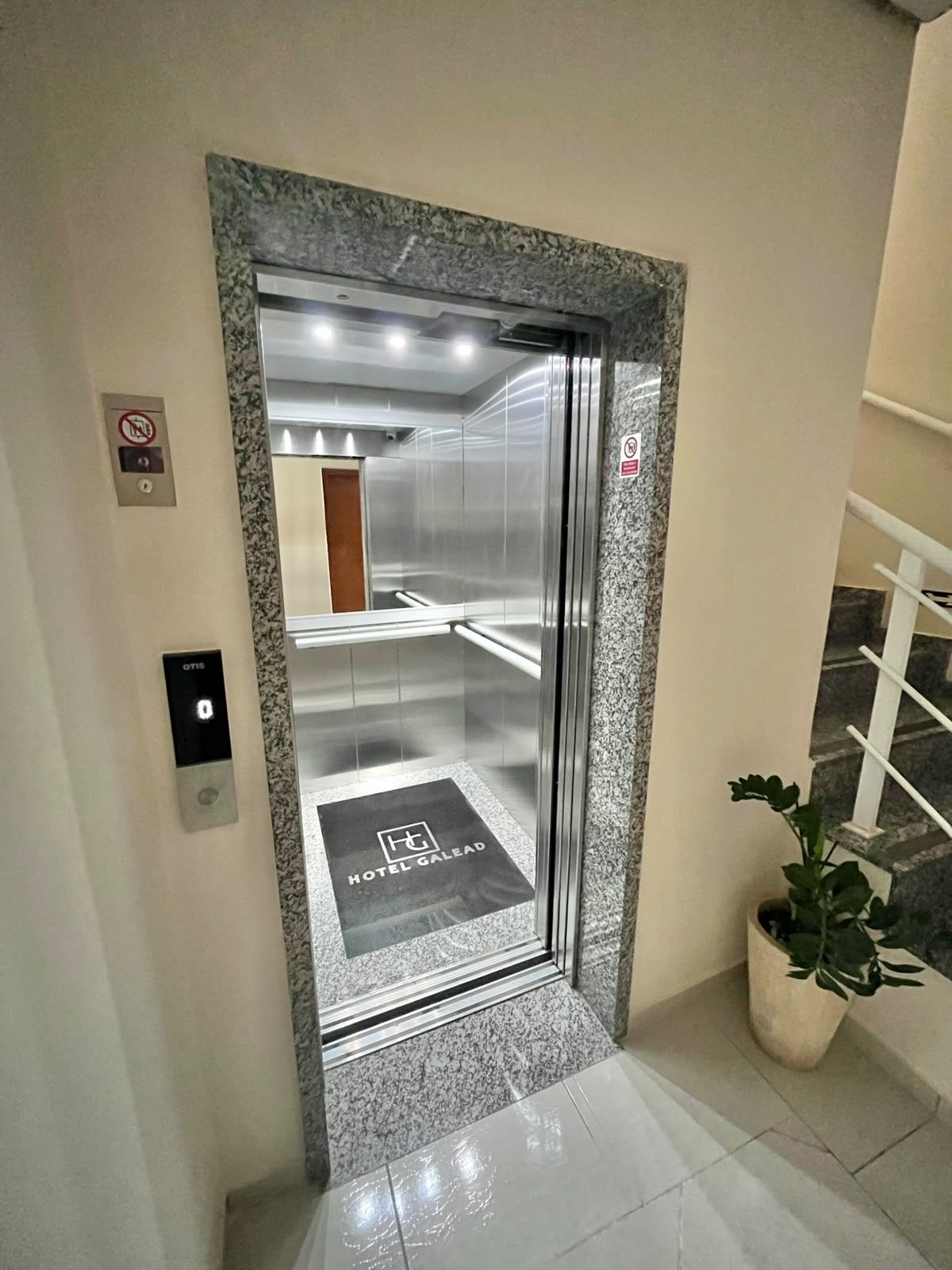 An elevator with a marble frame, a no-smoking sign, and a hotel name mat.