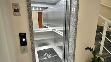 An elevator with a marble frame, a no-smoking sign, and a hotel name mat.