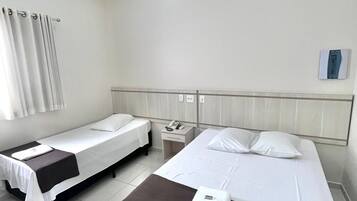 Habitación de hotel con dos camas individuales, una mesita de noche, un ventilador de techo y una ventana con cortinas.