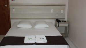 Habitación de hotel con cama, dos almohadas, mesita de noche con teléfono y controles remotos, y dos toallas dobladas sobre la cama.