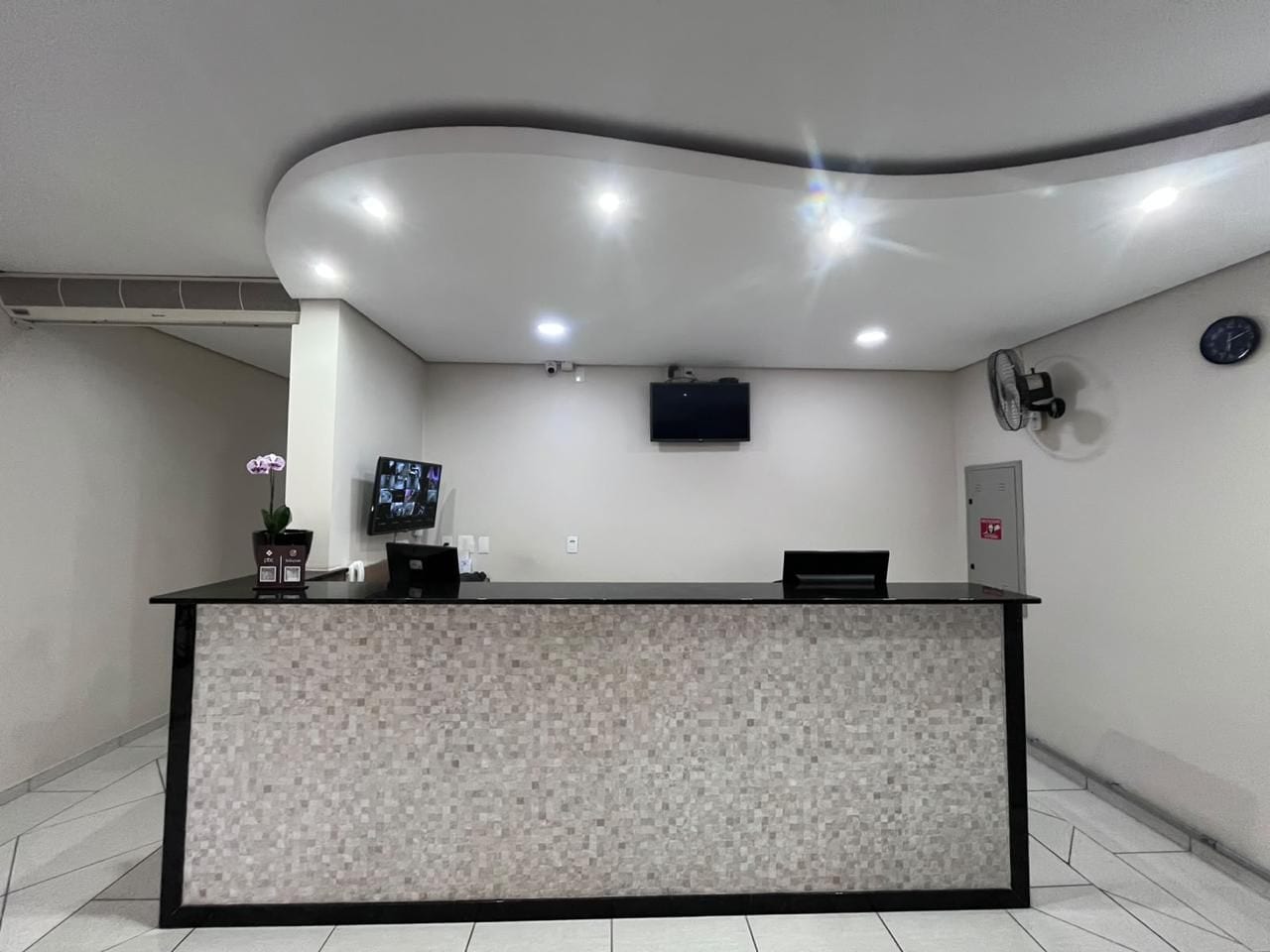 A reception desk with a tiled mosaic design, a flat-screen TV, and a wall-mounted clock.
