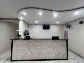 Balcão de recepção com design em mosaico de azulejos, uma TV de tela plana e um relógio fixado na parede.