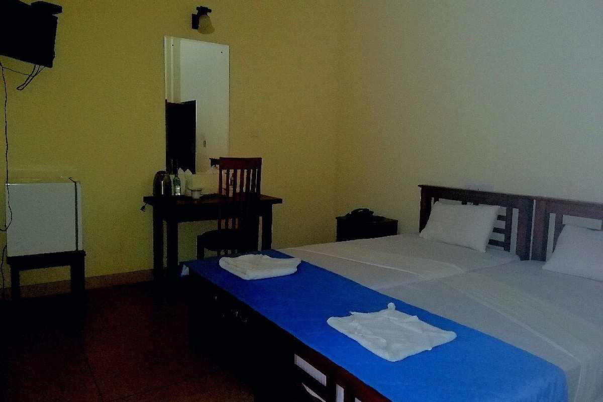A hotel room with a single bed, a desk with a chair, a small table, and a wardrobe.
