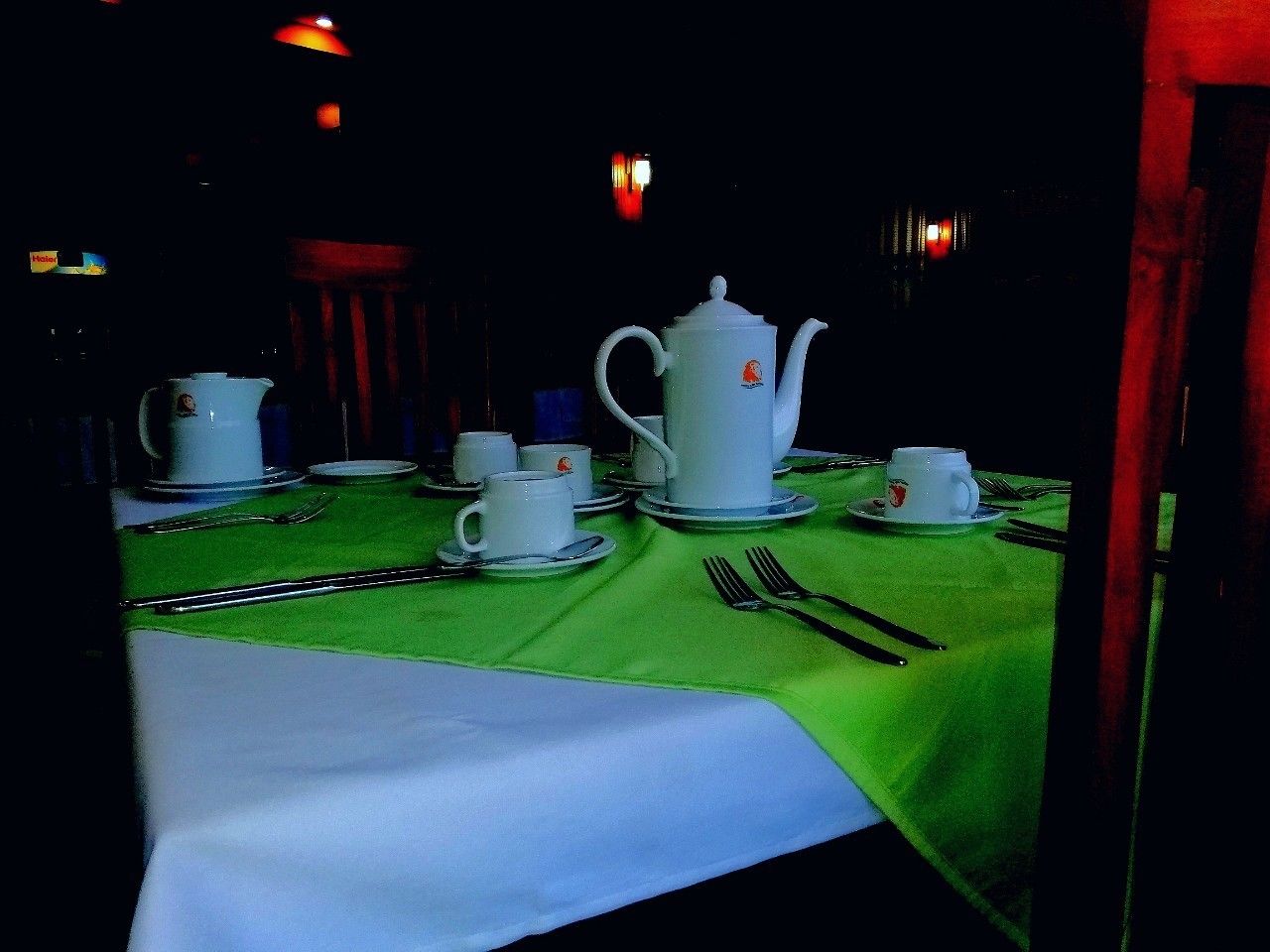 Una mesa dispuesta para servicio de té con teteras, tazas y platillos blancos, y un mantel verde.