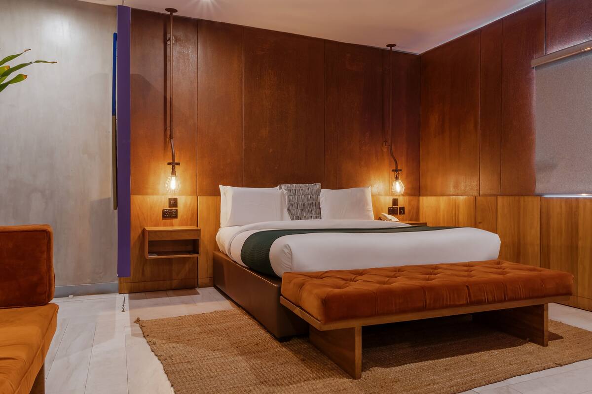 A modern bedroom with a wooden headboard, a large bed with white bedding, a wooden bench, and two bedside lamps.