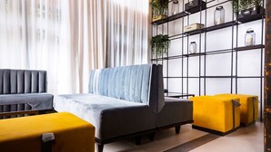 A modern living room with a grey sofa, yellow ottoman, and a black metal shelving unit against a white wall. - The Borough Lagos (Lekki)