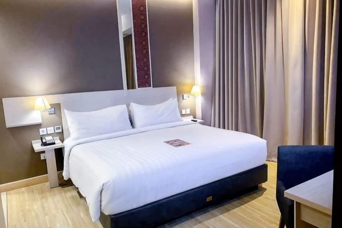 Quarto de hotel com uma cama grande, mesas de cabeceira, escrivaninha e uma cadeira.