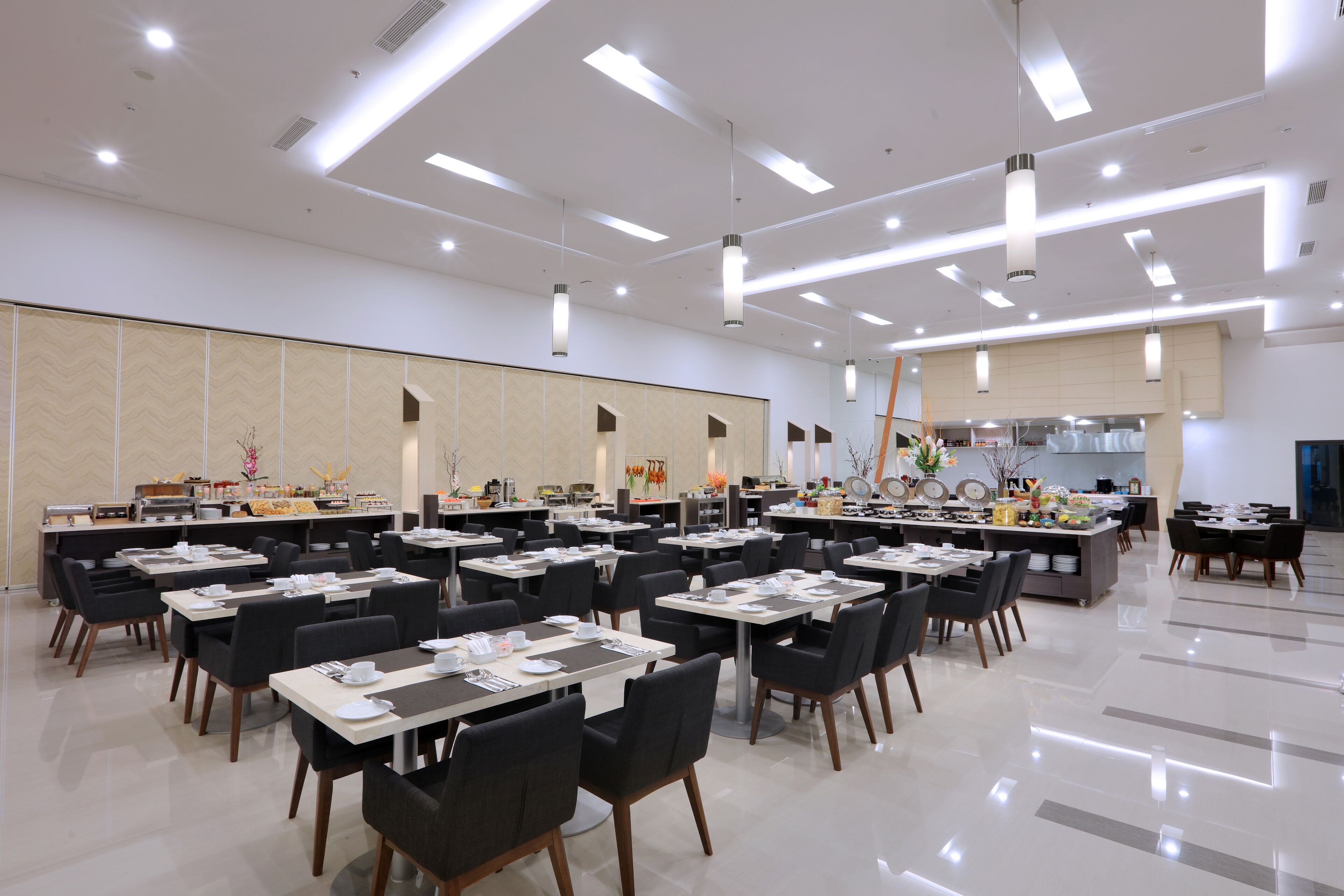 A spacious dining area with multiple tables and chairs, modern lighting fixtures, and a clean, polished floor.