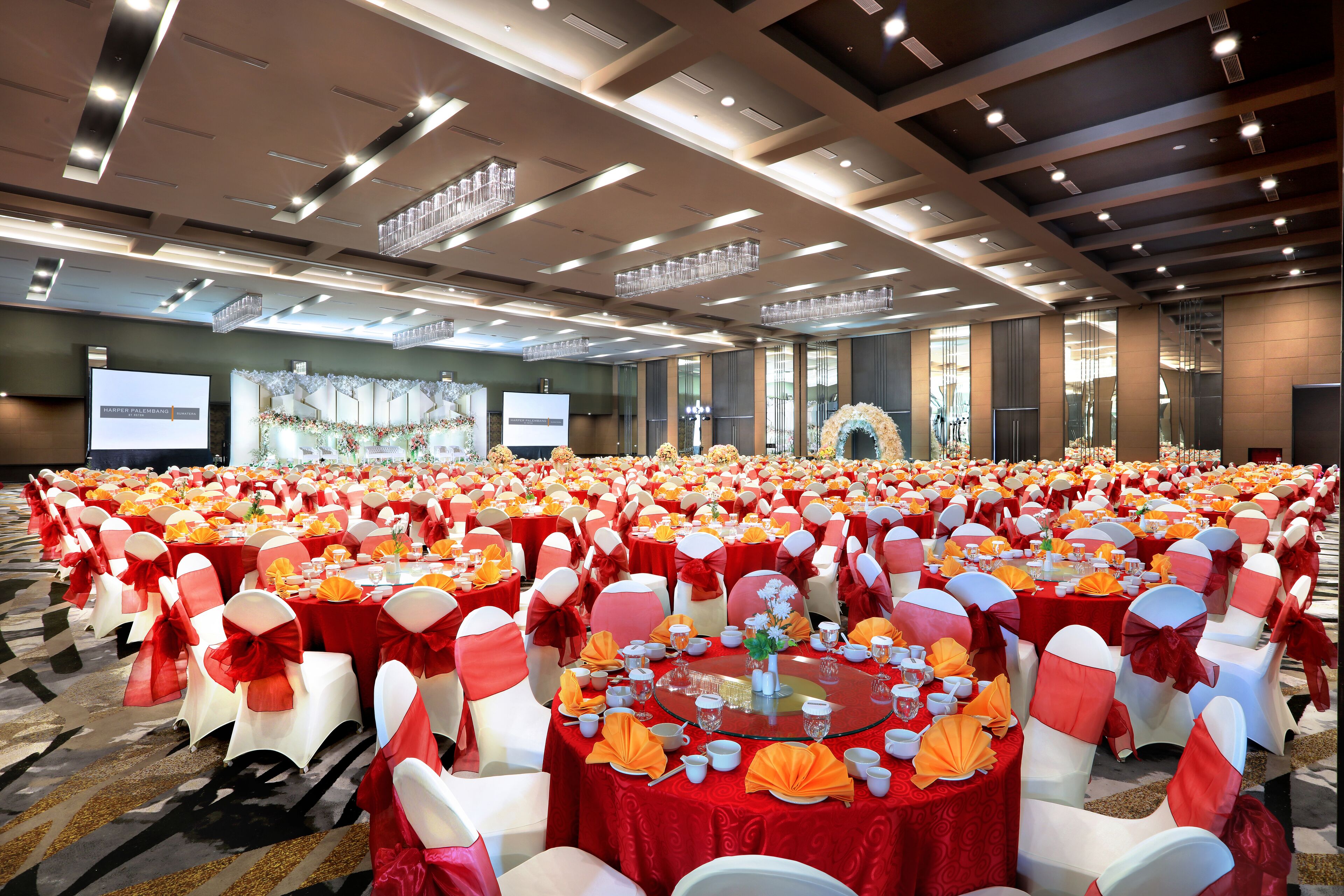 A banquet hall with round tables set for a formal event, featuring red tablecloths and white chairs with red sashes.