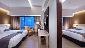 A hotel room with two beds, a desk, a chair, a TV, and a view of the city. - Harper Palembang by ASTON (Palembang)