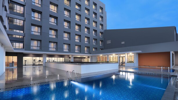 A modern hotel with a large indoor pool, a bar area, and a well-lit exterior. - Harper Palembang by ASTON (Palembang)
