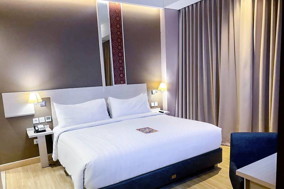 Quarto de hotel com uma cama grande, mesas de cabeceira com luminárias, uma escrivaninha e uma cadeira.