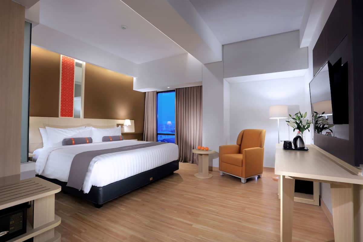 Quarto de hotel moderno com uma cama grande, uma escrivaninha, uma cadeira e uma televisão.