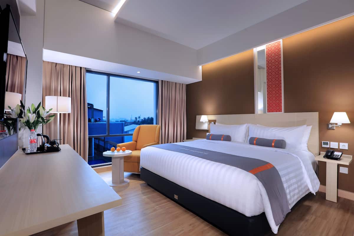 Quarto de hotel moderno com uma cama grande, uma escrivaninha, uma cadeira e vista para a cidade.