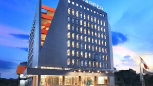 A modern hotel with a prominent 'HARPER' sign, featuring a large entrance, a well-lit facade, and a landscaped garden area. - Harper Palembang by ASTON (Palembang)