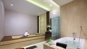 A modern bathroom with a large bathtub, a seating area, and a wooden vanity. - Harper Palembang by ASTON (Palembang)