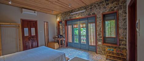 A room with two beds, a stone wall, wooden ceiling, and a door leading outside.