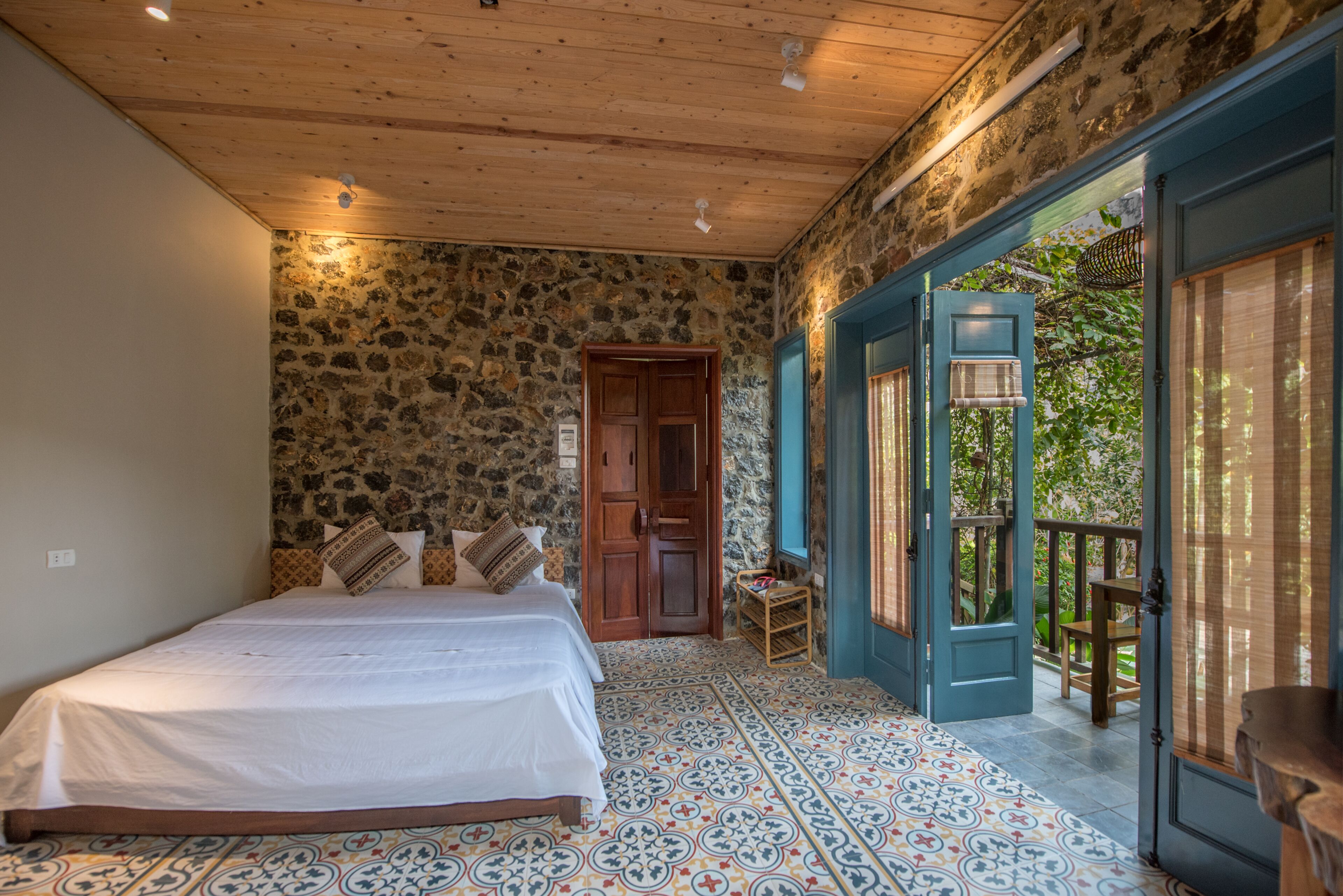 A bedroom with a stone wall, wooden ceiling, and a bed with patterned bedding.