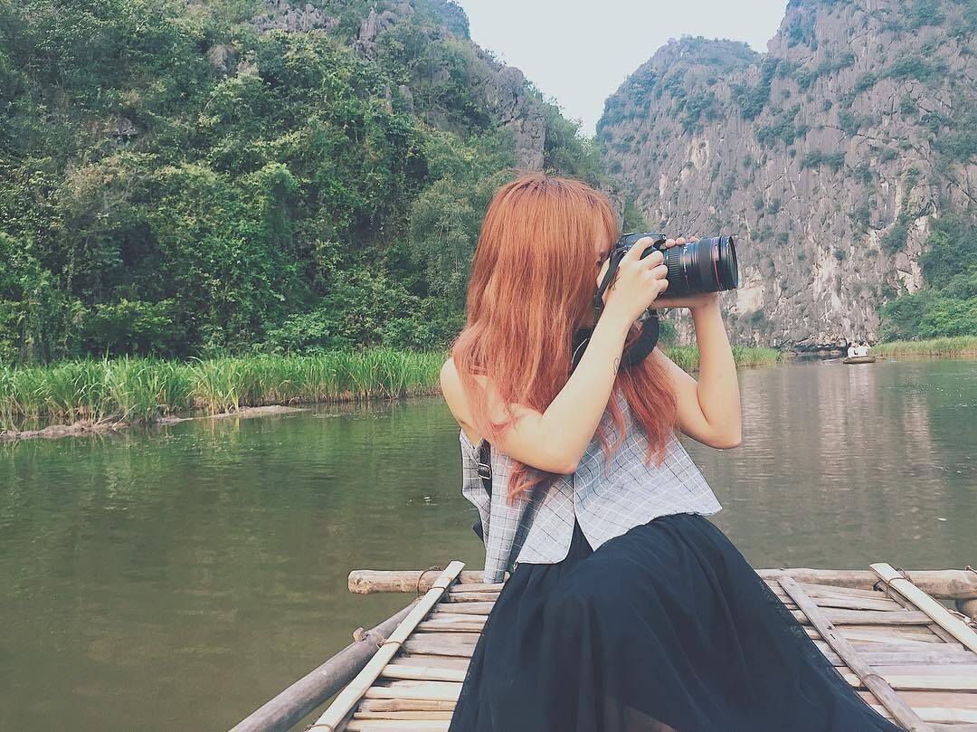 A person taking a photo with a camera on a wooden dock by a river.