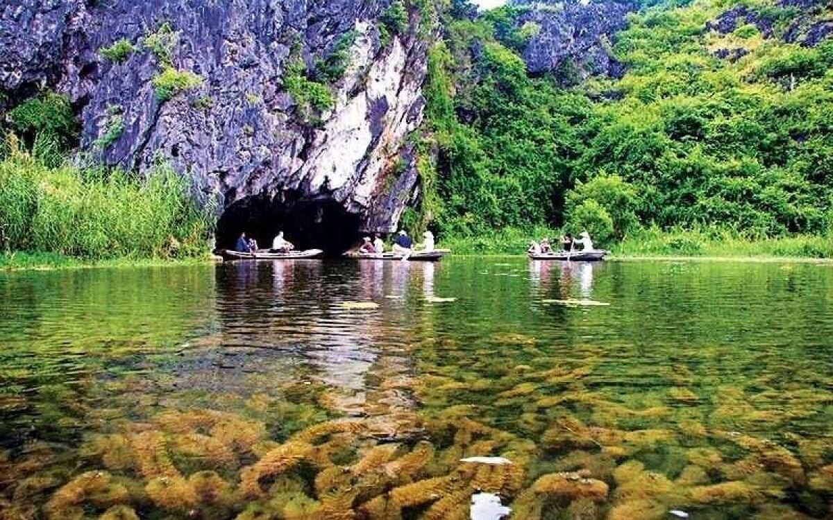 A cave entrance with boats on a clear river.