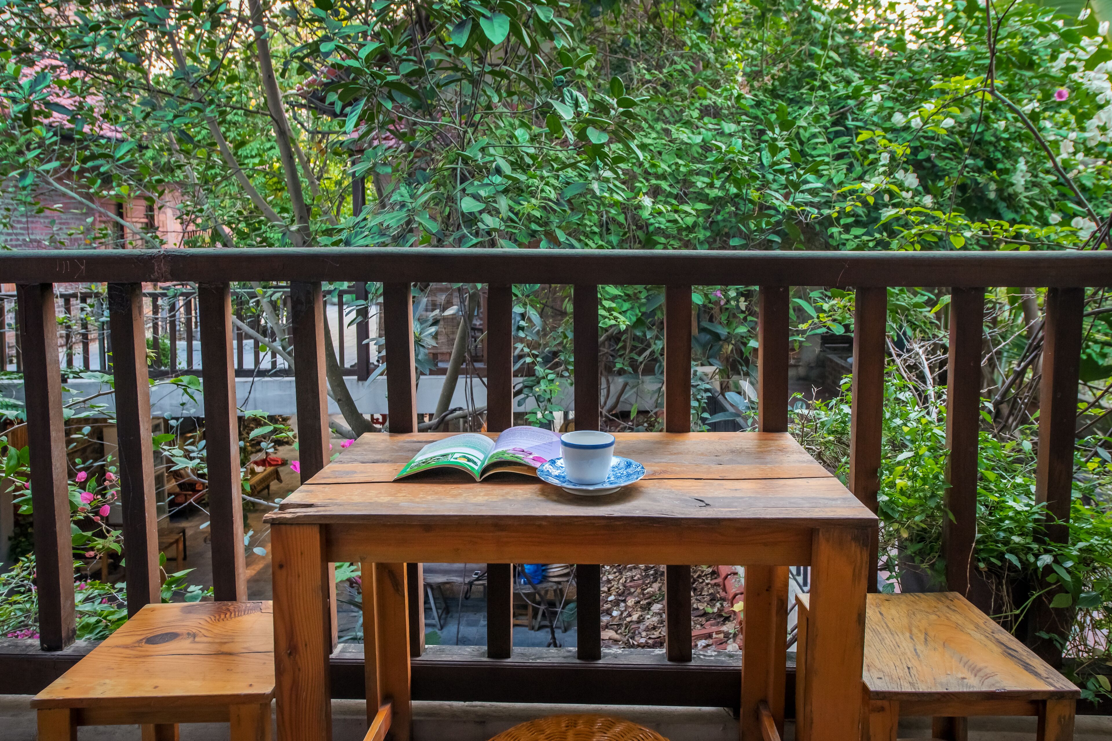 A wooden table with an open book and a cup on a balcony with a wooden railing.