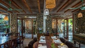 Un restaurante con un interior rústico que presenta vigas de madera a la vista, paredes de piedra y una gran mesa de comedor de madera dispuesta para una comida.