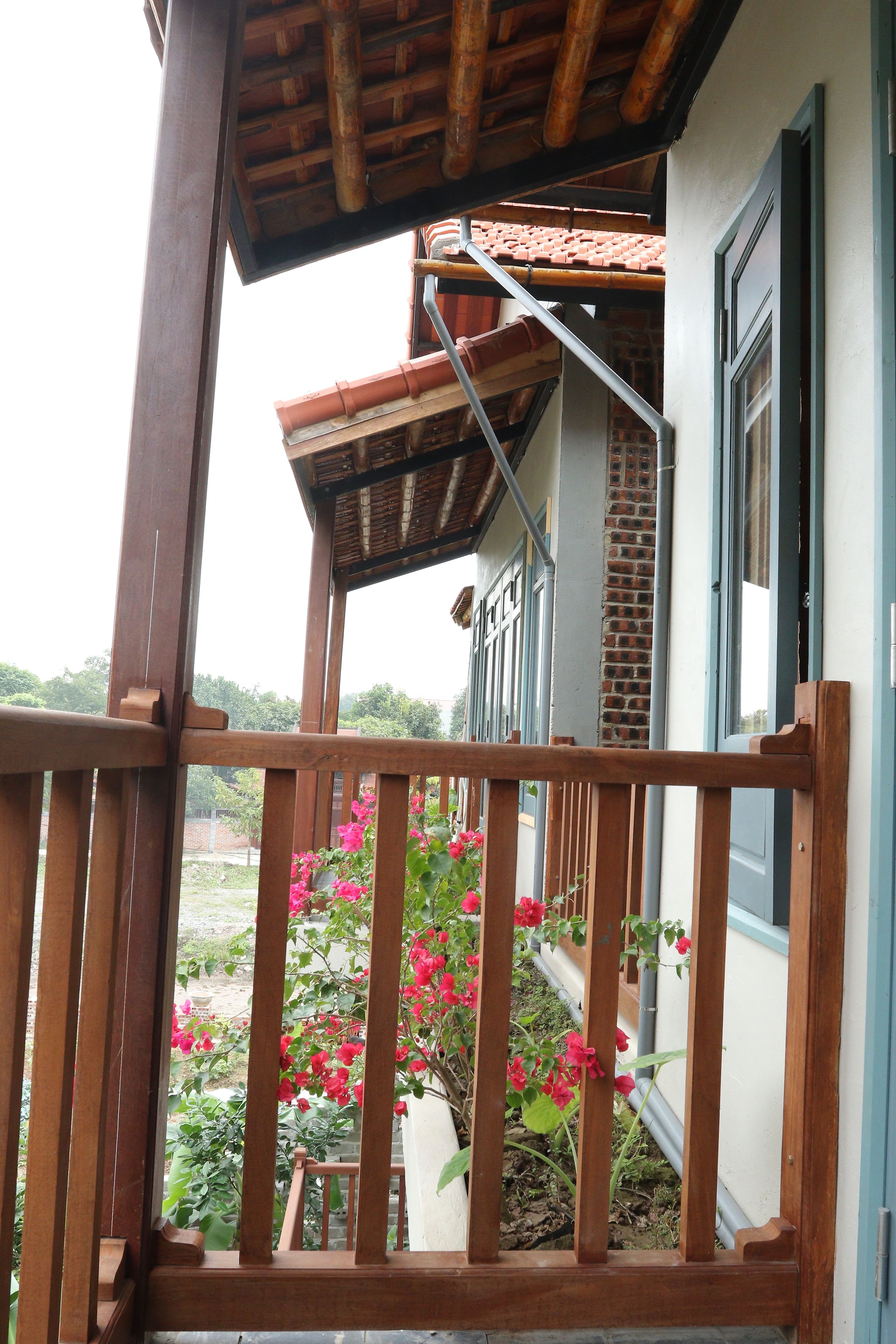 Un balcón de madera con vista a un jardín y un edificio con tejado de baldosas.
