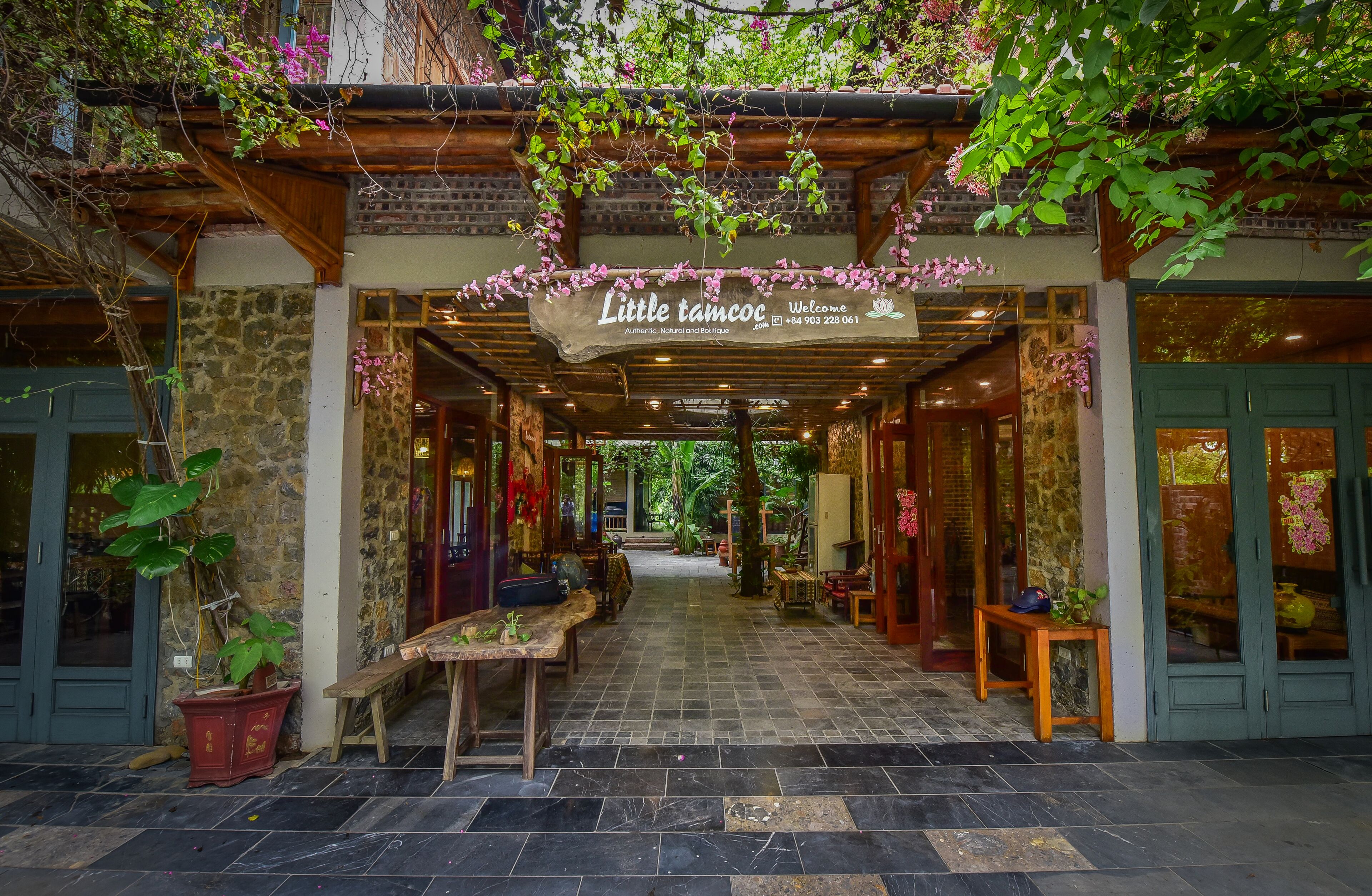 A covered entrance to a boutique hotel with a stone facade, wooden beams, and hanging plants.