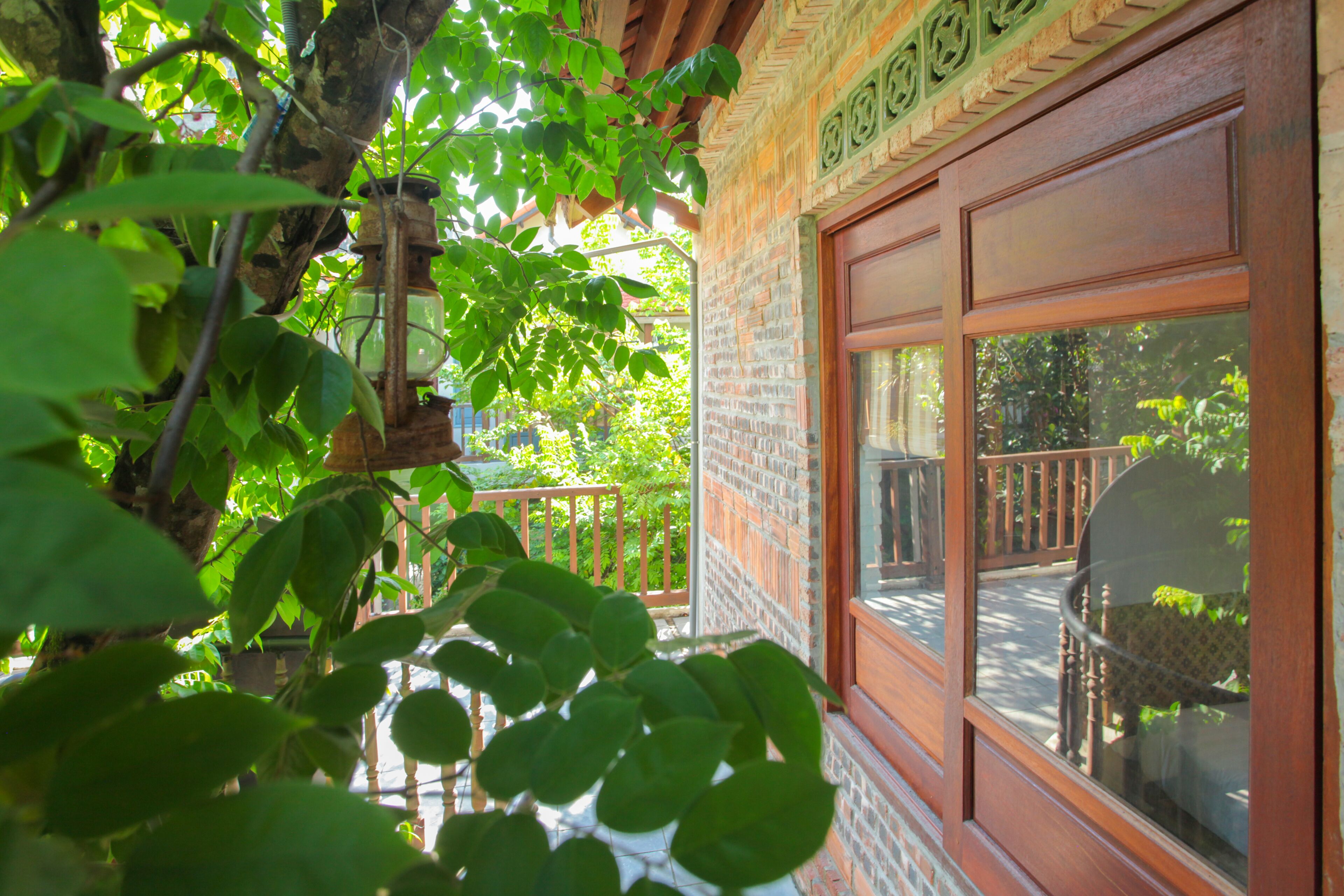 A wooden balcony with a brick wall, a wooden railing, and a view of greenery.