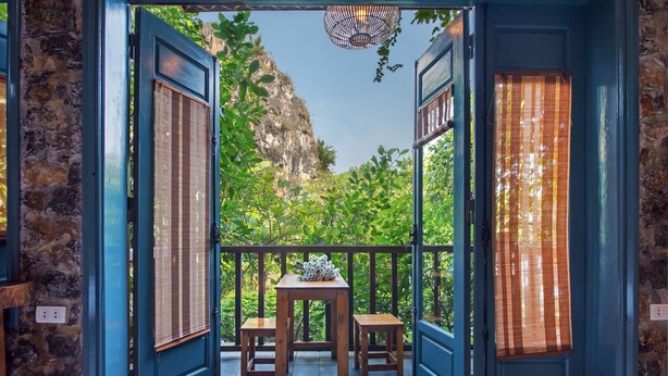 Un balcón con una mesa y dos sillas, vista a una montaña y una puerta azul con ventana.