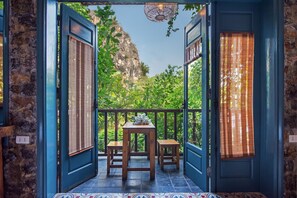 Un balcón con una mesa y dos sillas, vista a una montaña y una puerta azul con ventana.