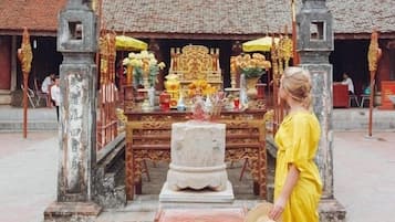 A person in a yellow dress walking past a temple with a traditional roof and ornate decorations.