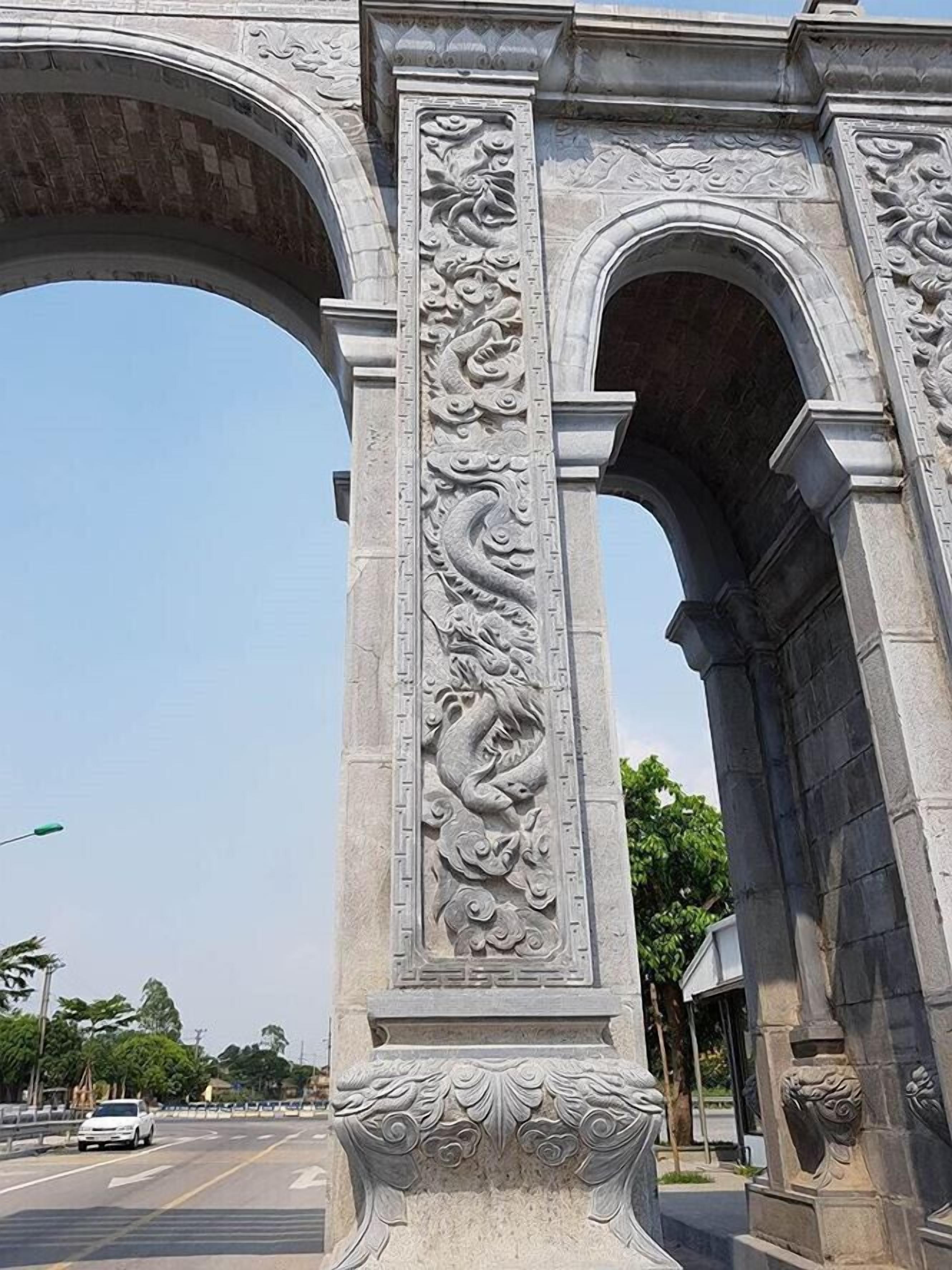 A stone archway with intricate carvings, including a dragon motif, and a clear sky in the background.