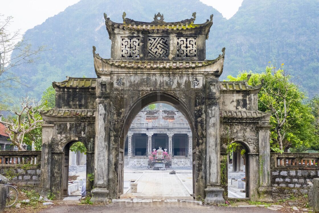 Un antiguo arco de piedra con intrincados grabados y un techo tradicional, que conduce a un complejo de templos.